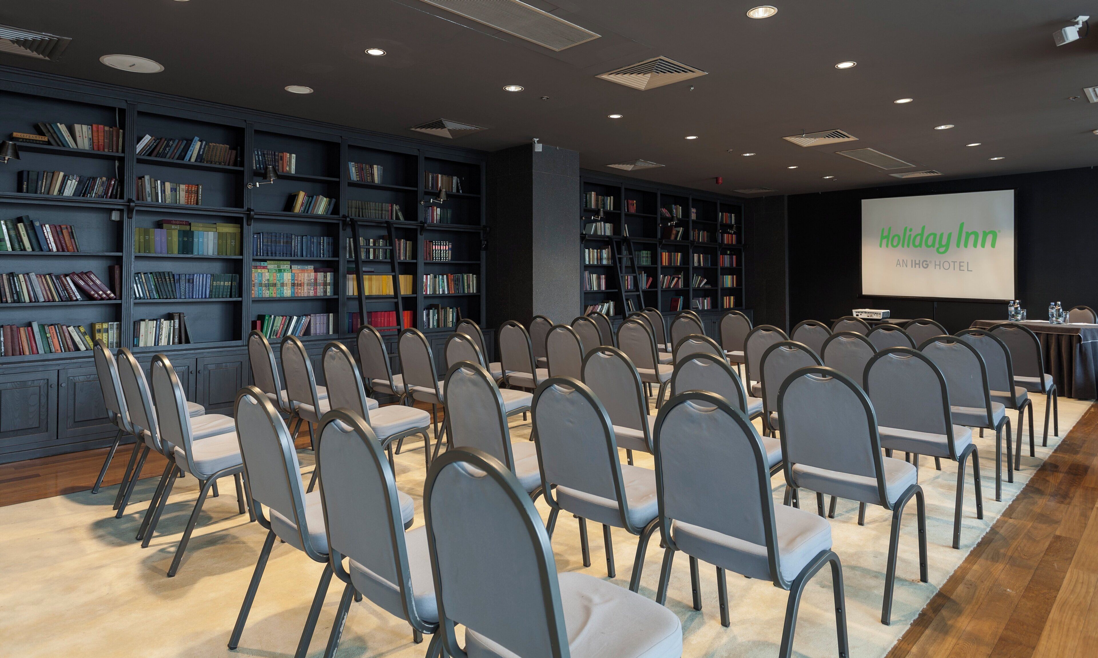 A conference room with rows of chairs, a projector screen, and bookshelves filled with books.