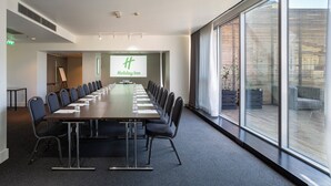 Un salón de conferencias con una larga mesa, sillas y una pantalla de proyección que muestra 'Holiday Inn'.