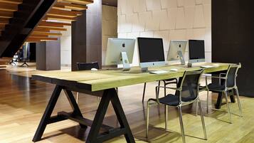 A modern office space with a long wooden table, four Apple iMac computers, and two black office chairs.