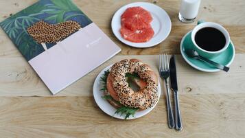 Un desayuno con un bagel, pomelo, café y una libreta sobre una mesa de madera.