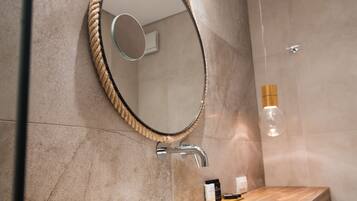 A bathroom with a wooden vanity, a round mirror with a rope frame, a white sink, and a shower area with a wooden door.
