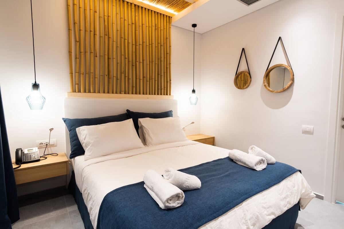 Un lit bien fait, avec une literie bleue et blanche, une tête de lit en bois et deux tables de chevet avec des lampes.