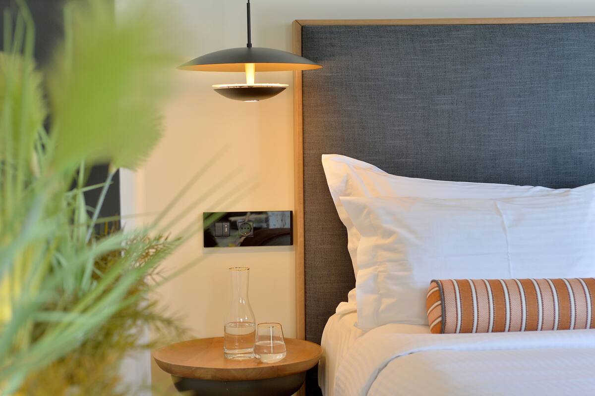 Une chambre d’hôtel avec un lit, une table de chevet avec une lampe, un vase et un verre.
