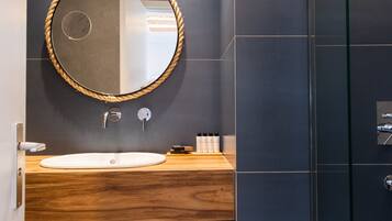 A modern bathroom with a wooden vanity, a round mirror with a rope frame, and a glass shower enclosure.