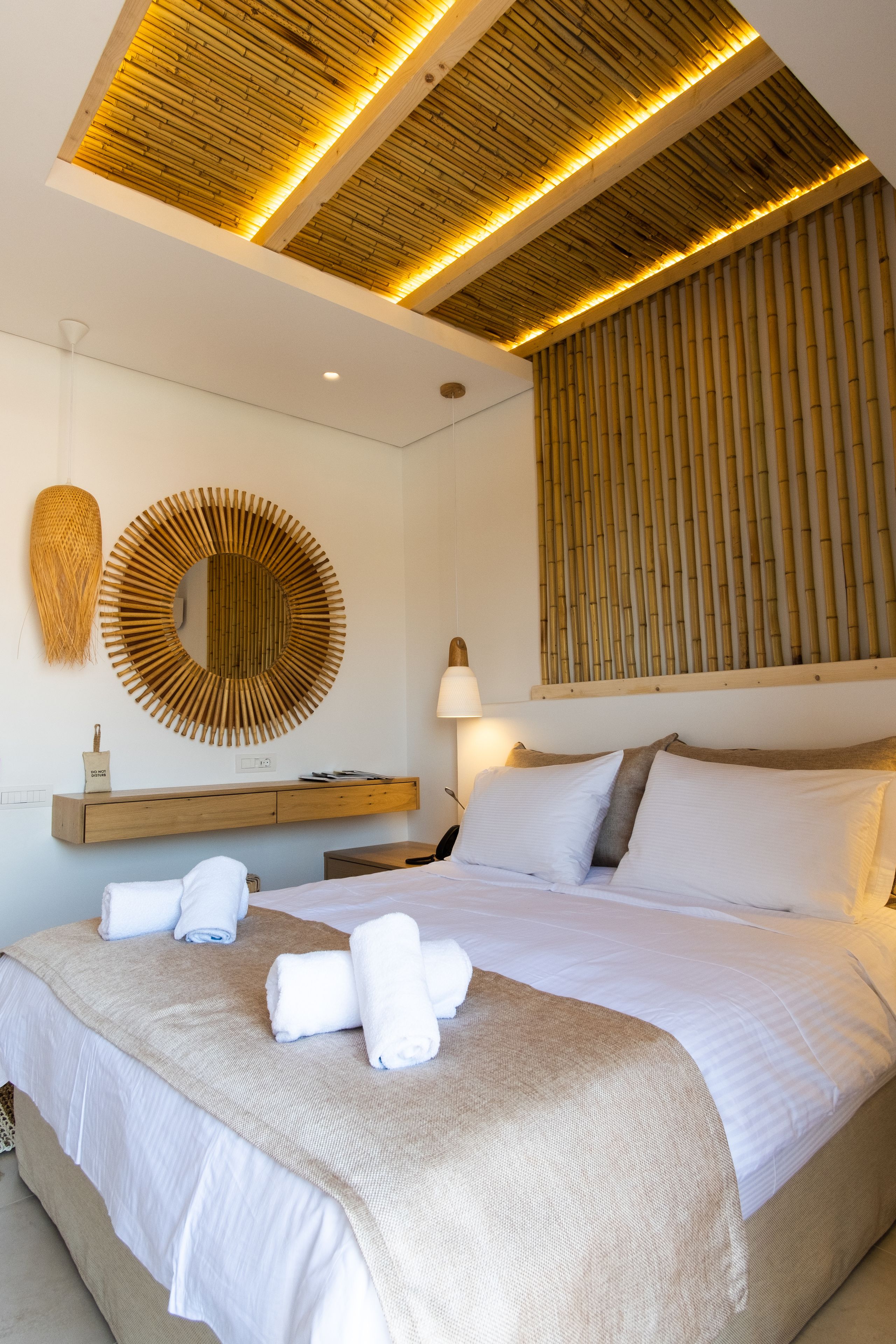 A modern hotel room with a large bed, a round mirror, a wooden headboard, and a wall-mounted lamp.