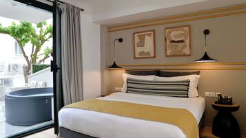 Una habitación de hotel con una cama, una mesita auxiliar, una lámpara de pared y un gran ventanal con cortinas.