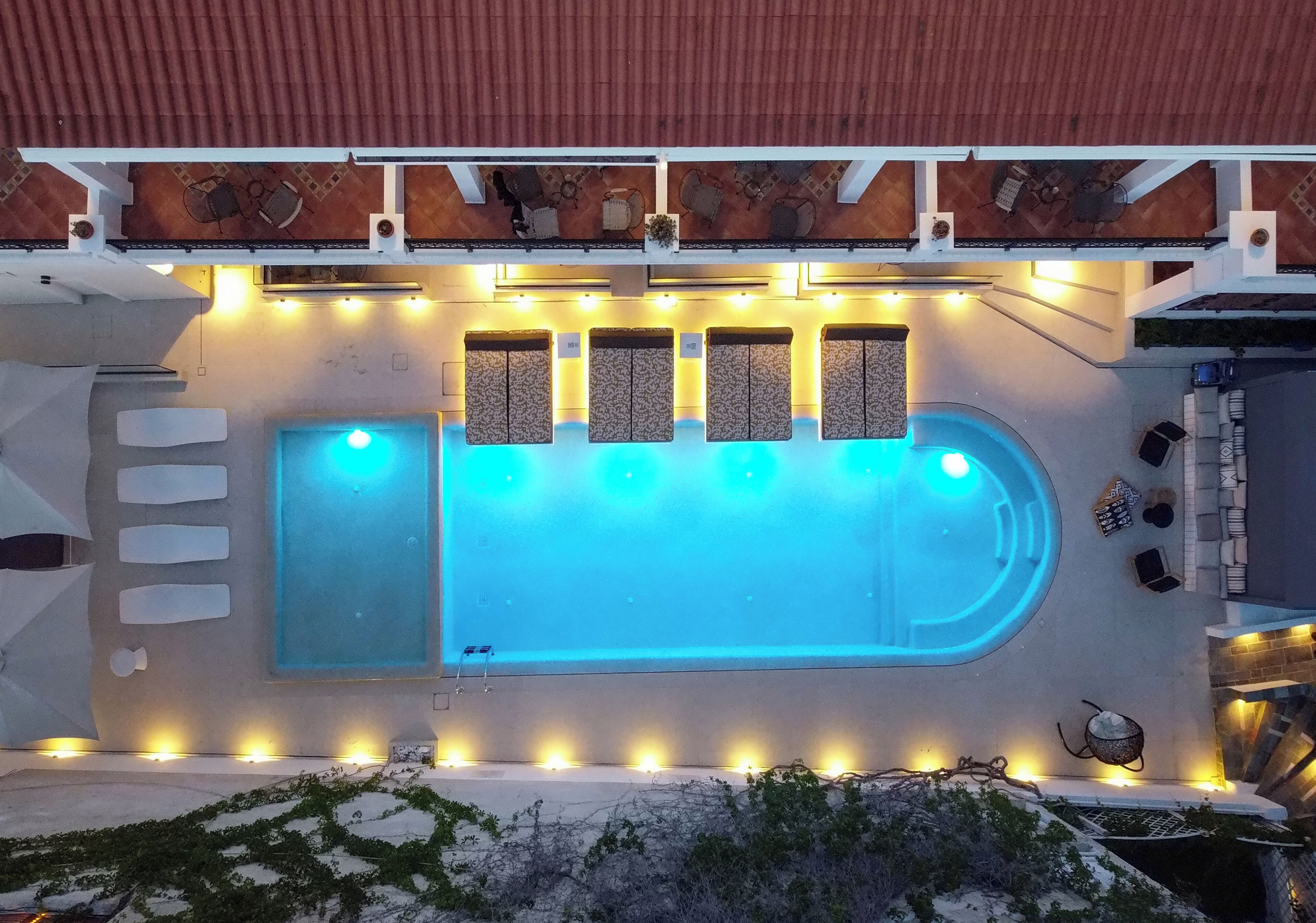 Una piscina exterior con un jacuzzi integrado, rodeada de zonas de estar y un porche cubierto.