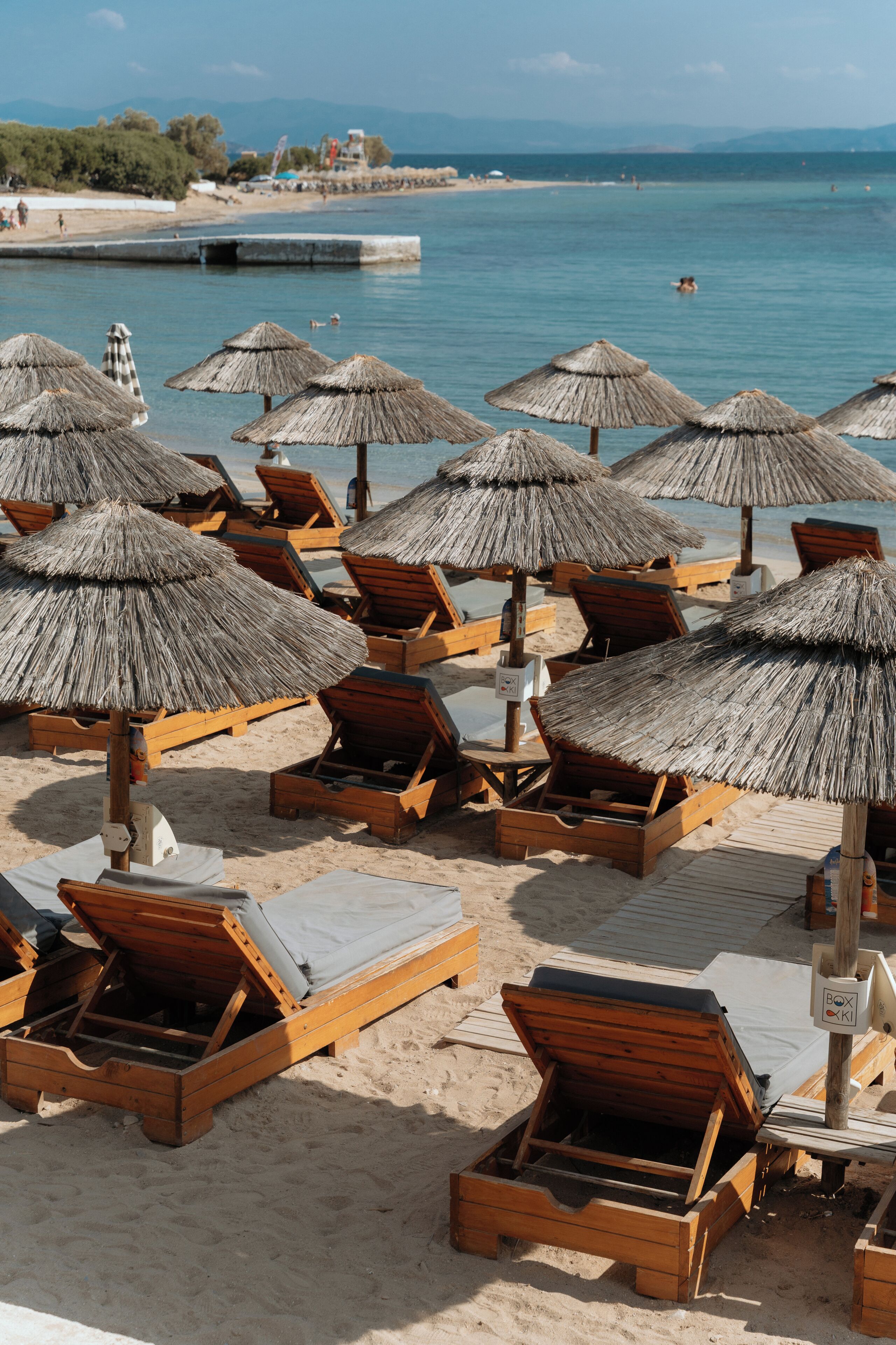 Una playa con sillones de madera y sombrillas de paja.