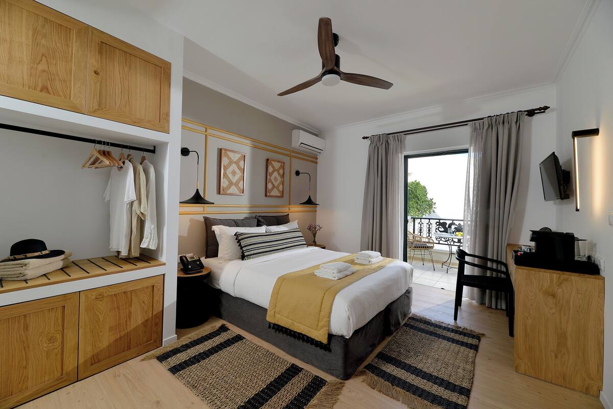 Une chambre à coucher comprenant un lit, une table de chevet, une armoire, un ventilateur de plafond et une vue sur l’extérieur.