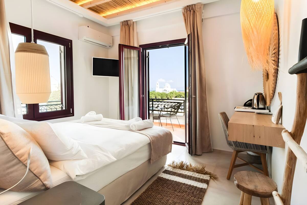 Une chambre à coucher avec un lit, un bureau et une vue sur un bâtiment, visible à travers une porte ouverte.