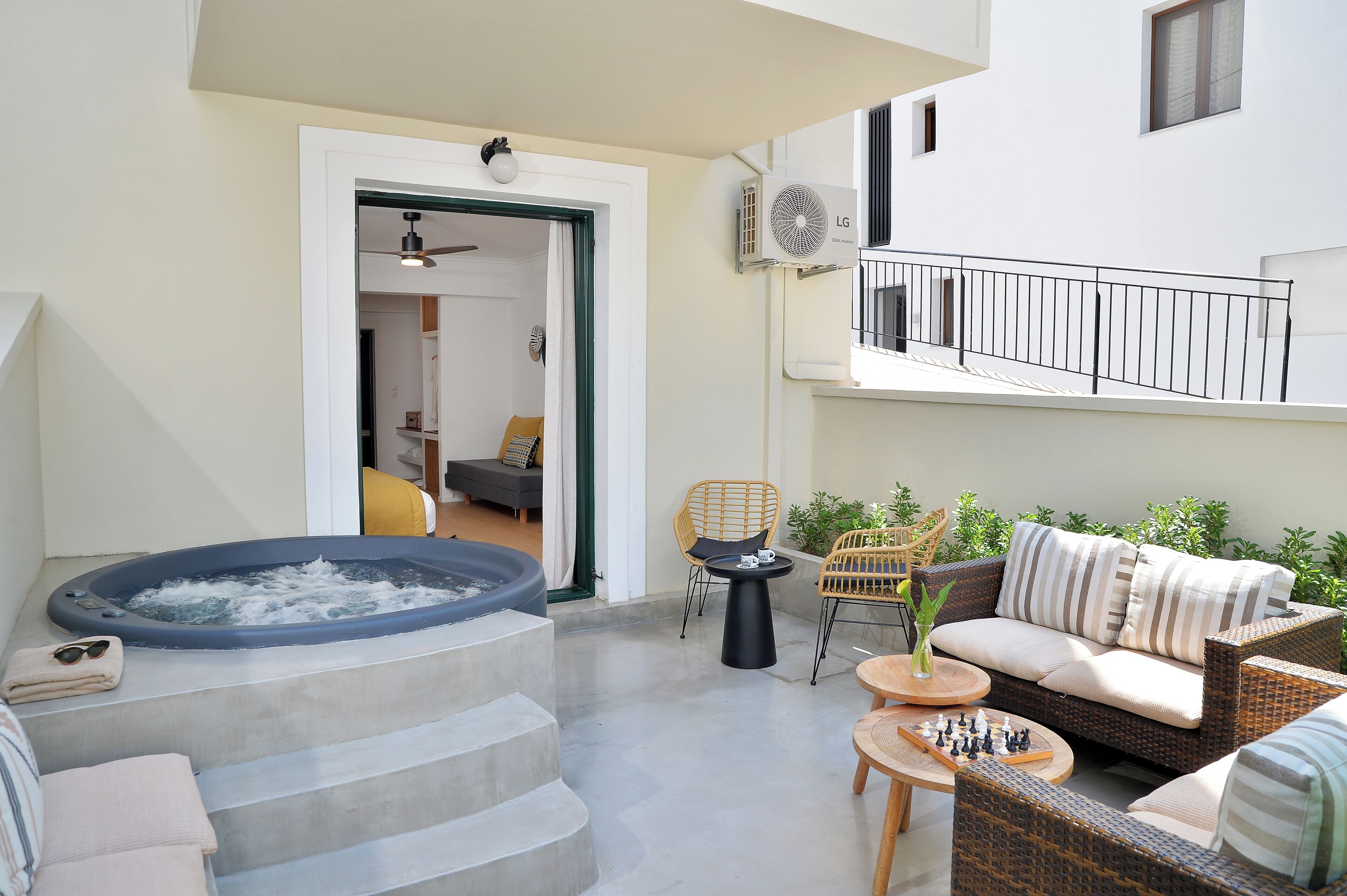 Ein moderner Außenbereich mit Whirlpool, Korbmöbeln und einem Balkon.