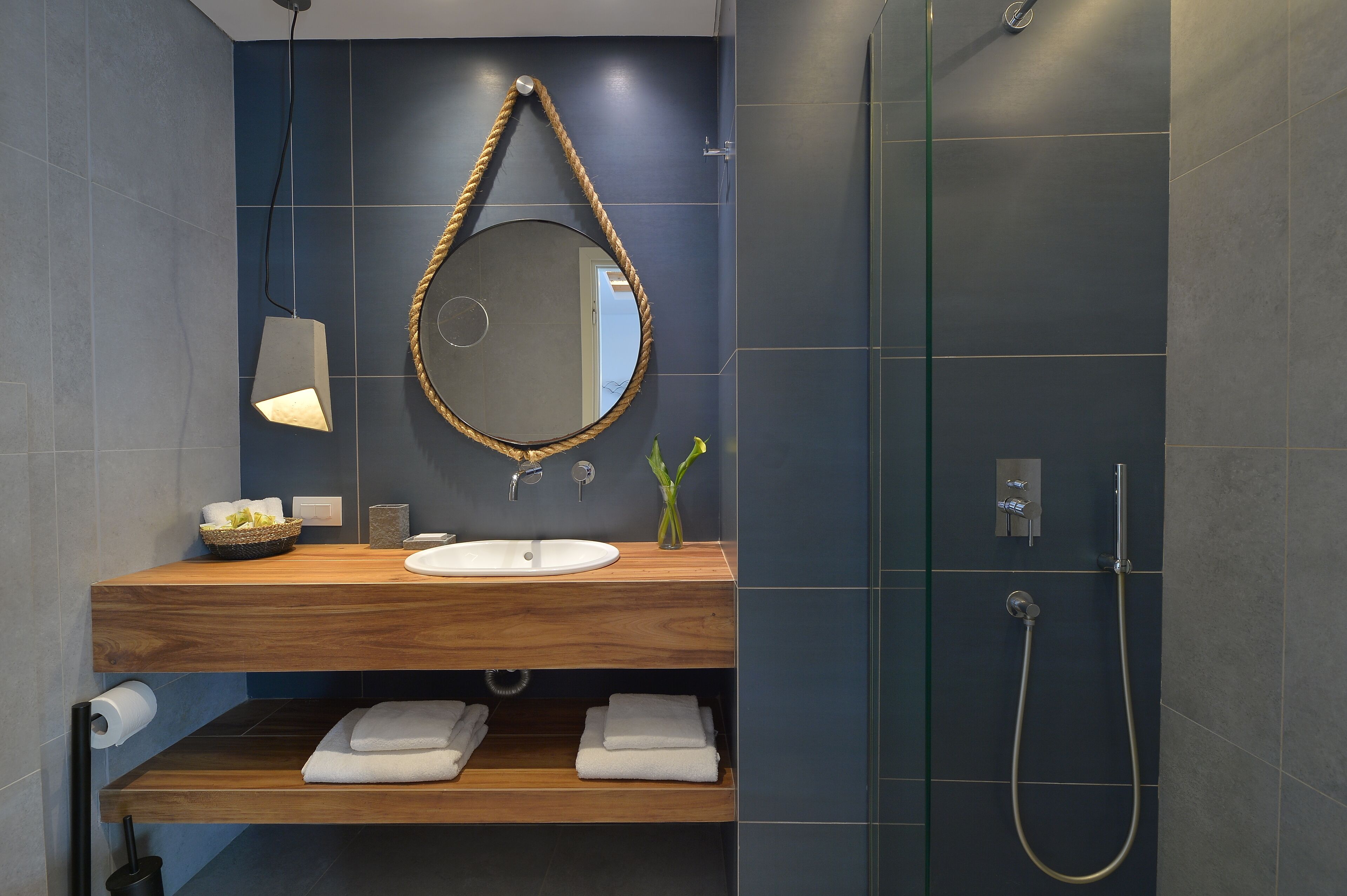 A modern bathroom with a wooden vanity, a round mirror, a white sink, and a glass-enclosed shower.