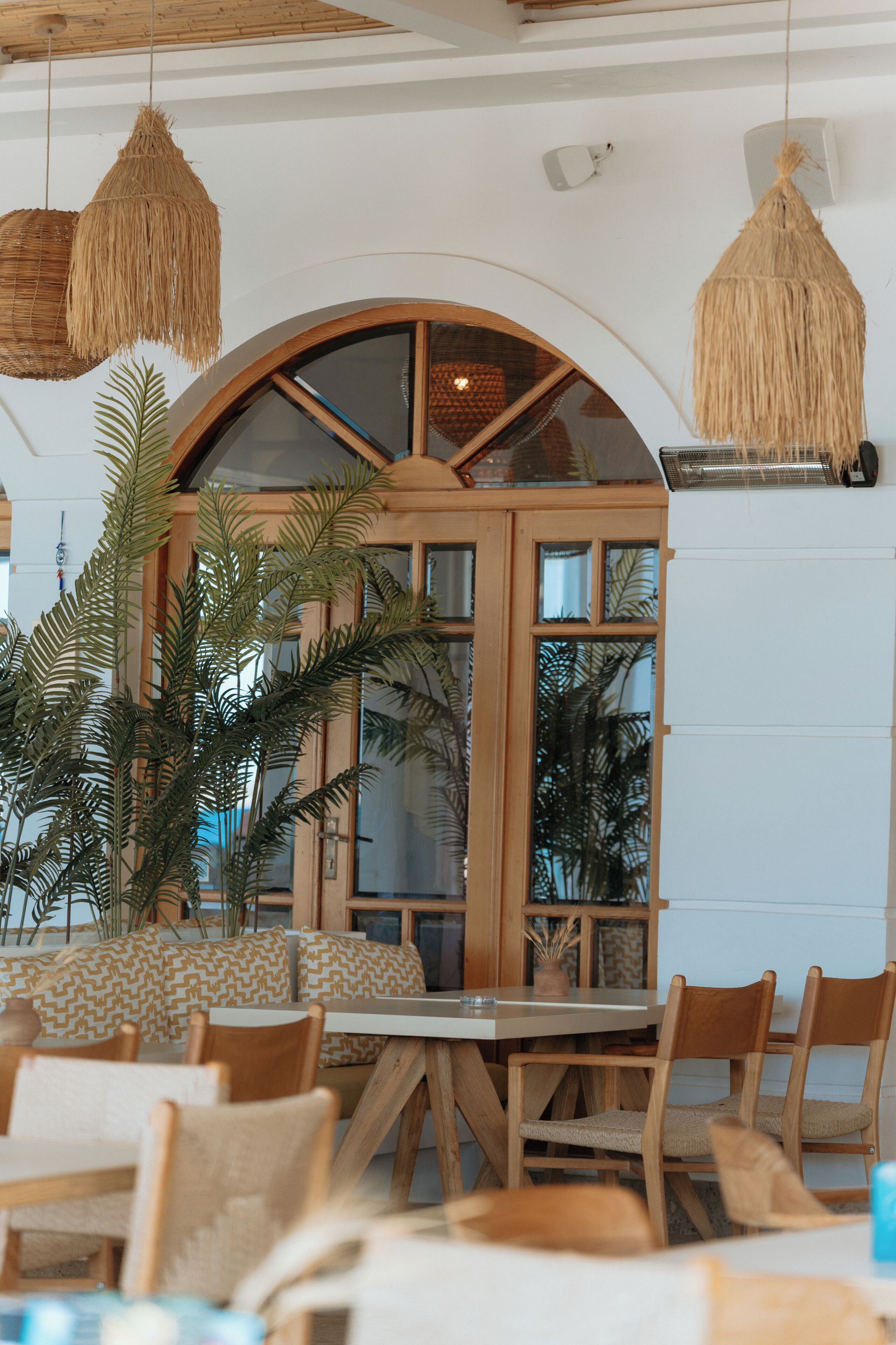L’intérieur d’un restaurant avec une table et des chaises en bois, une grande porte en arc et des luminaires suspendus en forme de suspensions tissées.