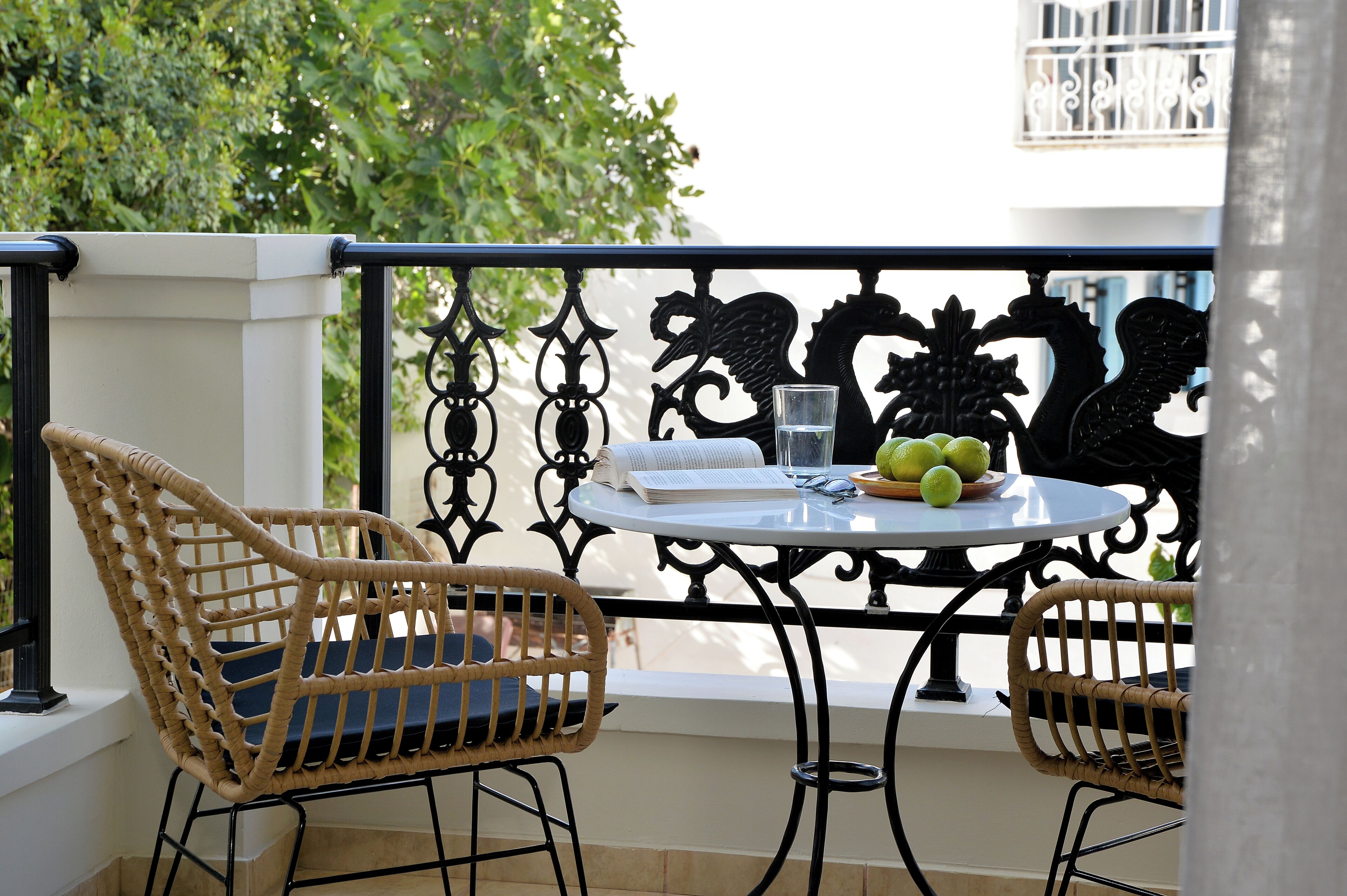 A balcony with wicker chairs, a round table with a glass of water, and a fruit bowl.
