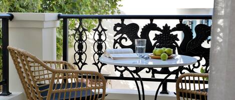 A balcony with wicker chairs, a round table with a glass of water, and a fruit bowl.