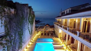 A poolside area with a long swimming pool, lounge chairs, and a view of the sea.