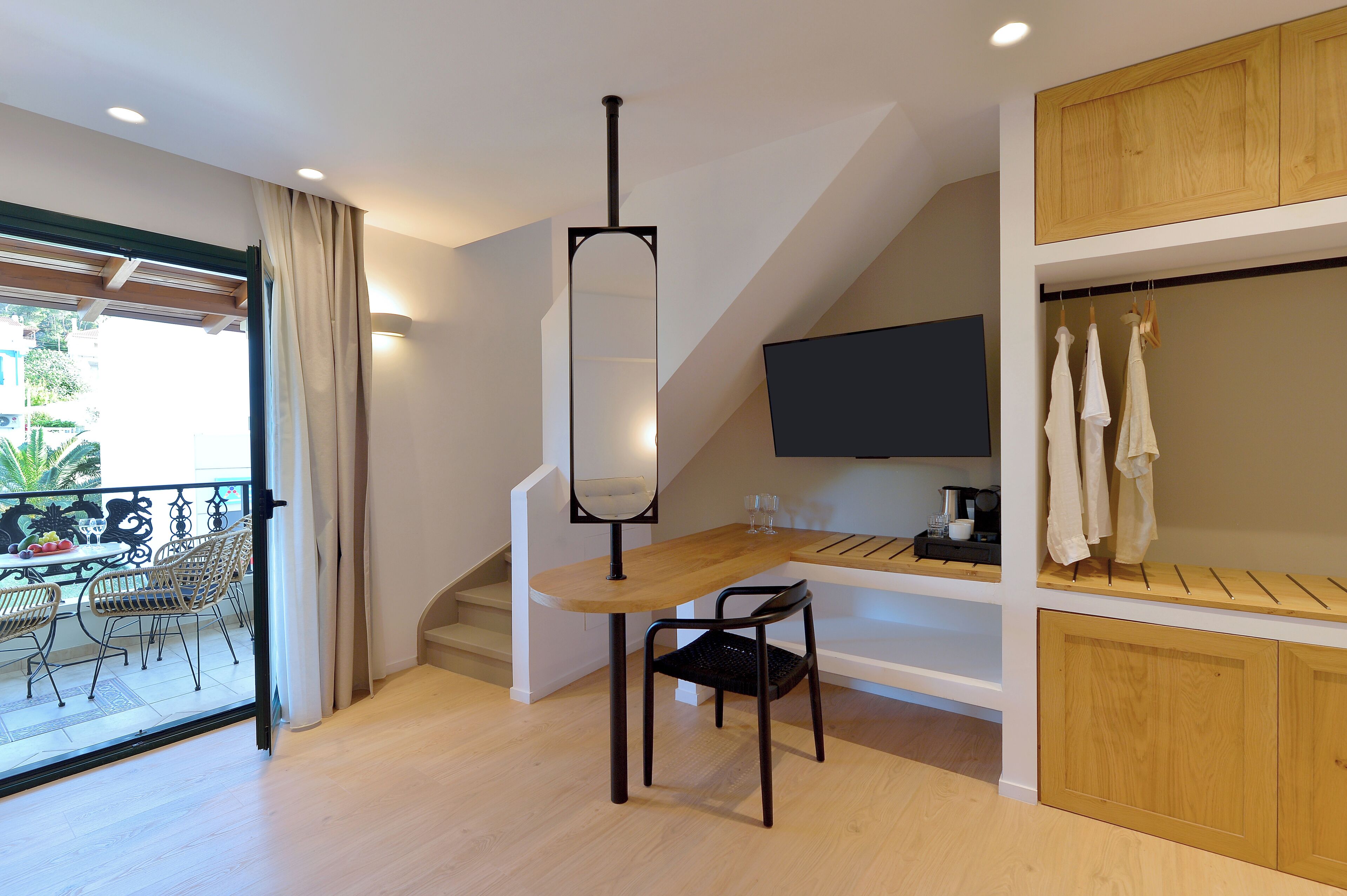 A modern room with a dining area, a TV mounted on the wall, and a balcony with outdoor furniture.