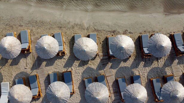 An aerial view of a beach with rows of sun loungers and large umbrellas.