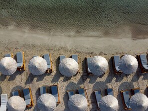 Une vue aérienne d’une plage avec des rangées de transats et de grands parasols.