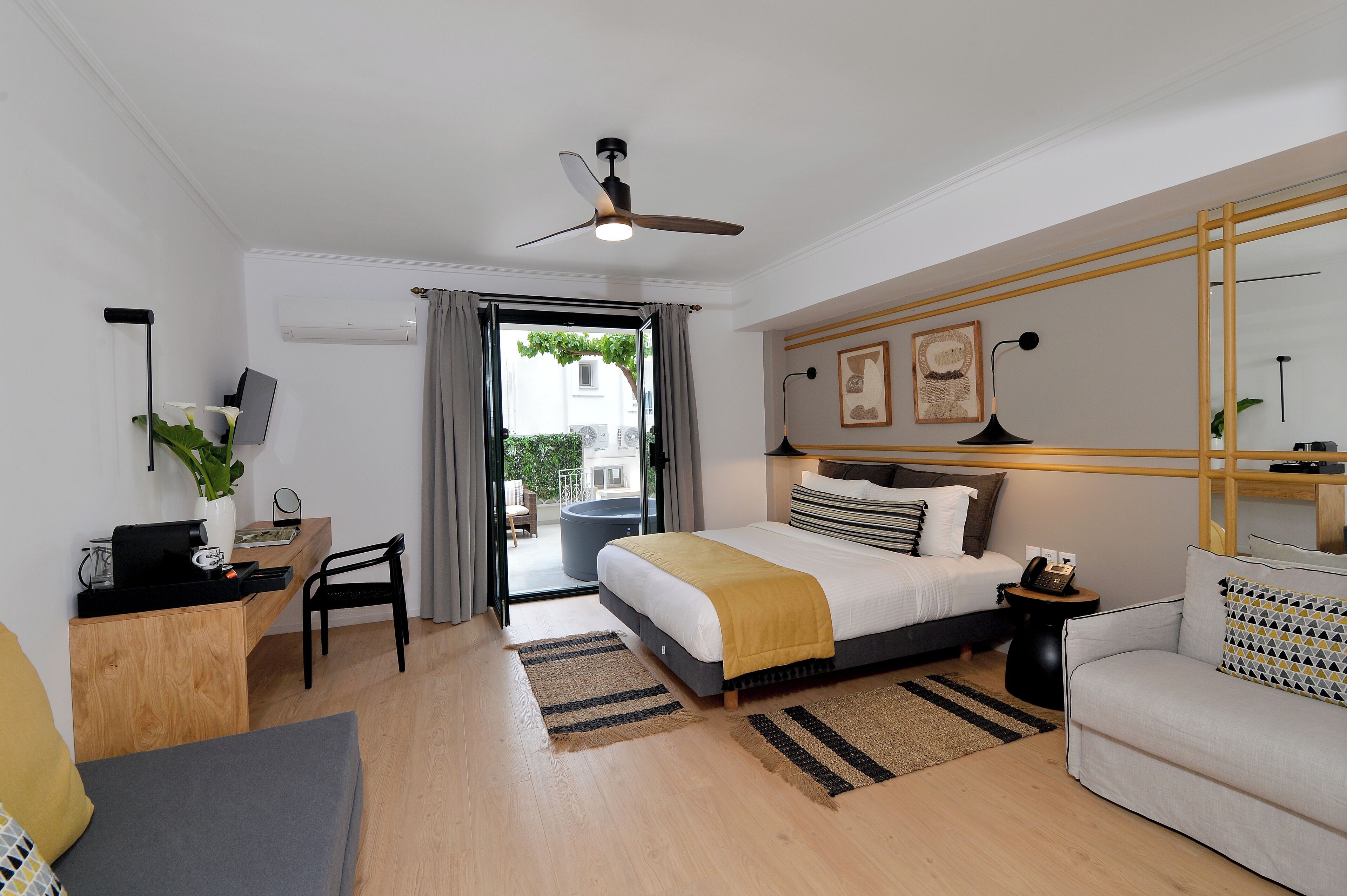 A modern hotel room with a bed, a desk, a chair, a sofa, and a balcony with a view.