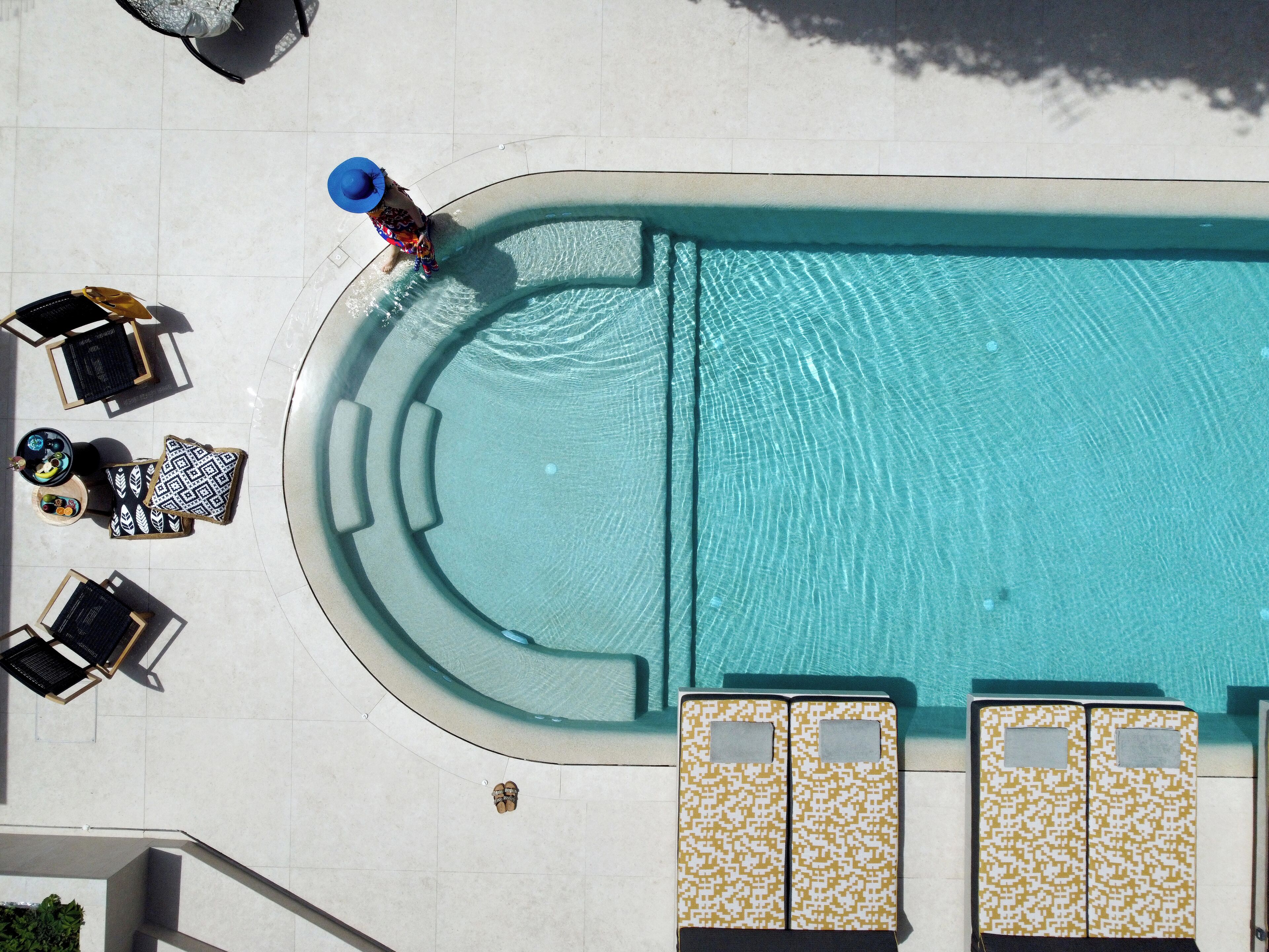 A top-down view of a swimming pool area with lounge chairs, a sunbed, and a small seating area.