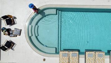A top-down view of a swimming pool area with lounge chairs, a sunbed, and a small seating area.