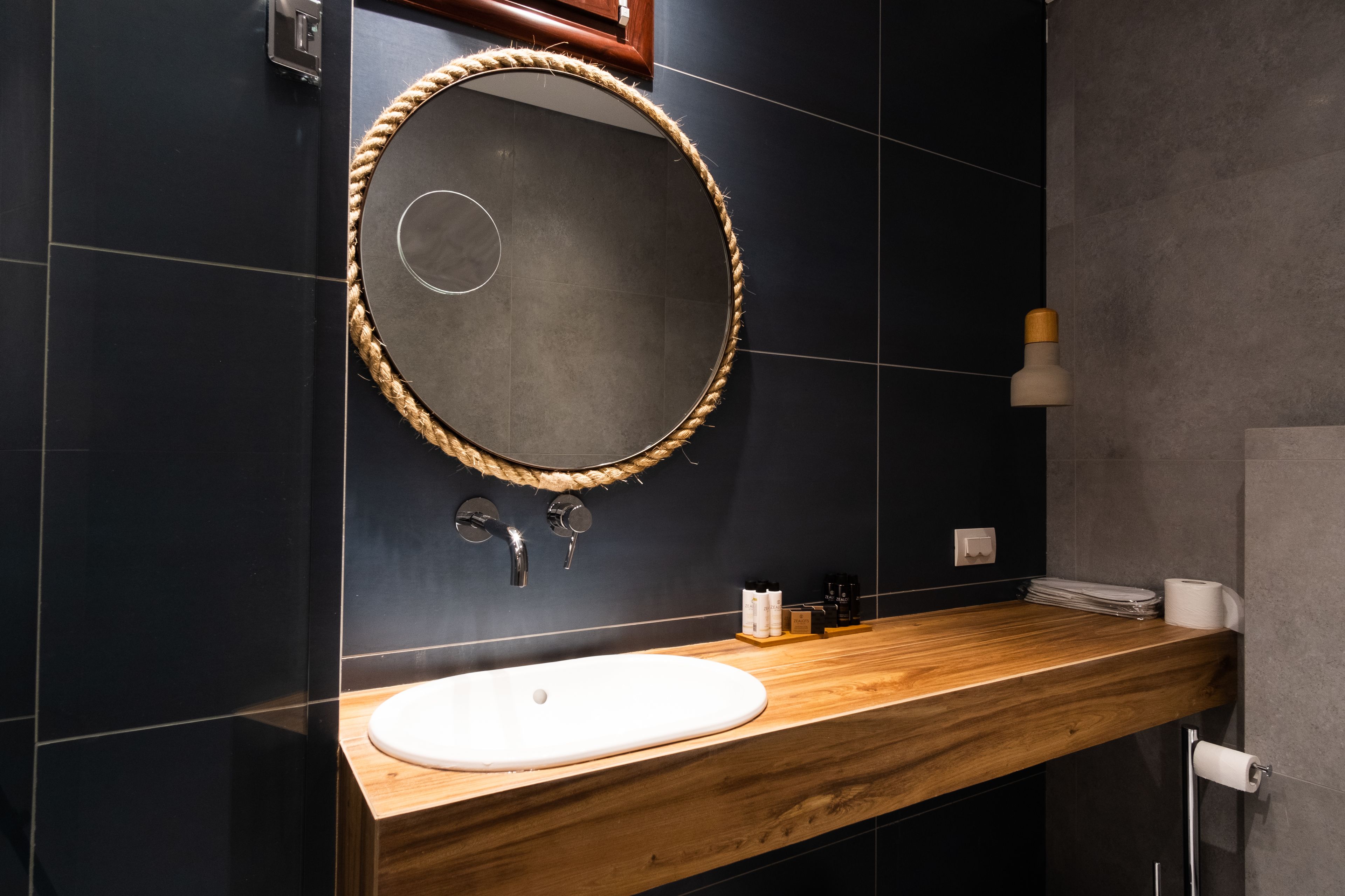 A bathroom with a wooden vanity, a round mirror with a rope frame, a white sink, and a towel rack.