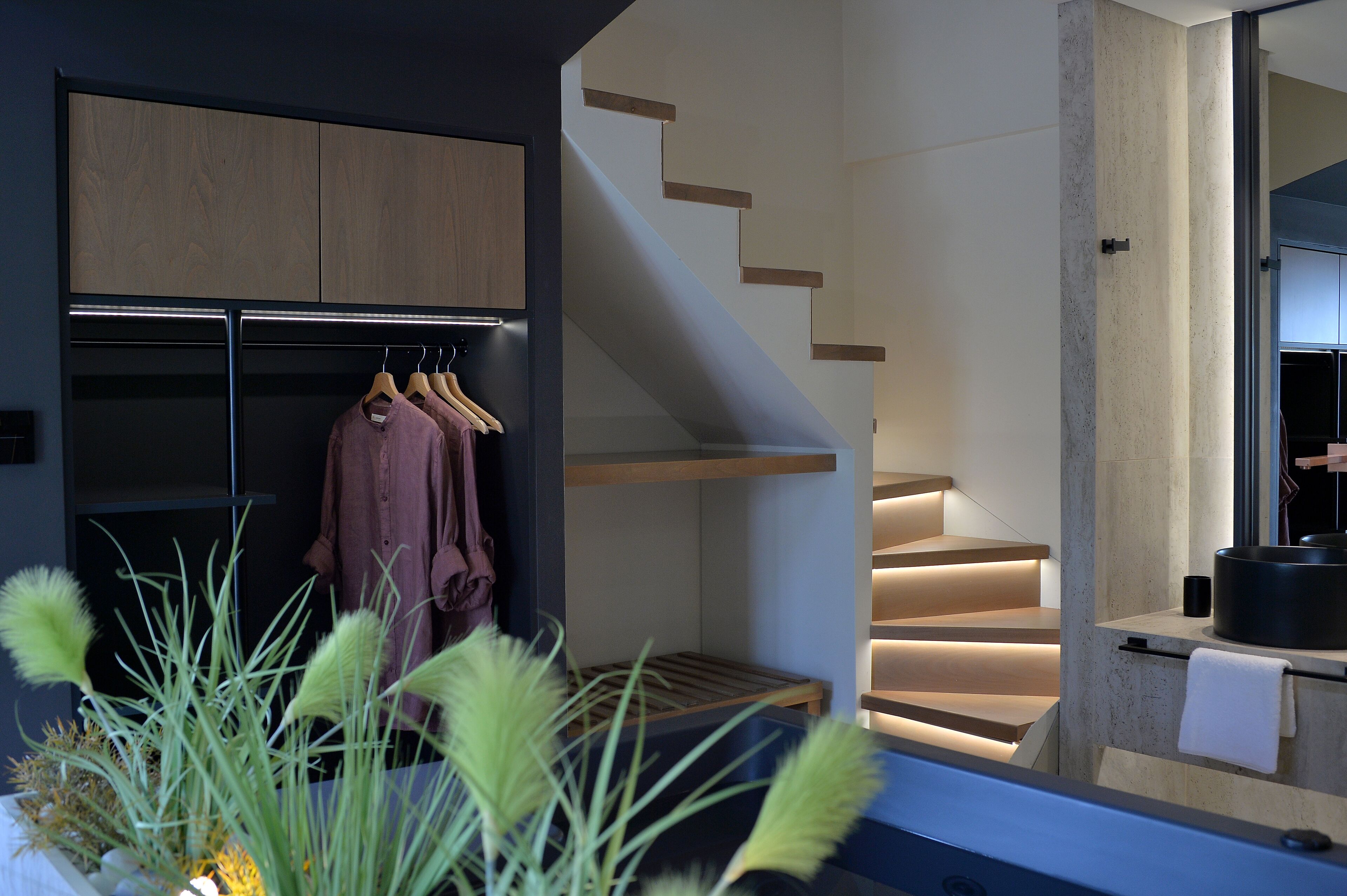 A modern interior with a wooden wardrobe, a staircase with integrated lighting, and a small seating area.