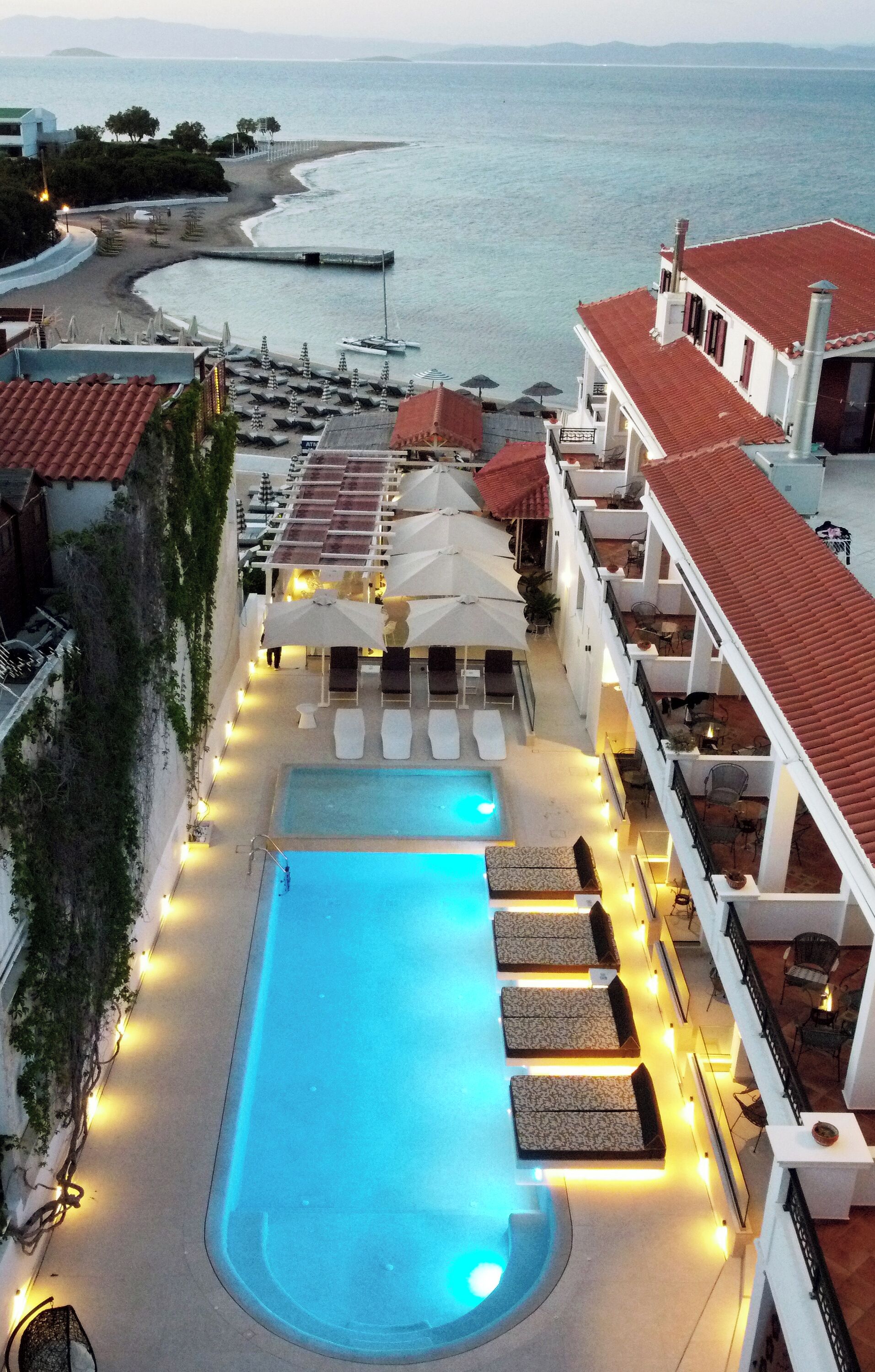A hotel with a pool, lounge chairs, umbrellas, and a view of the sea.