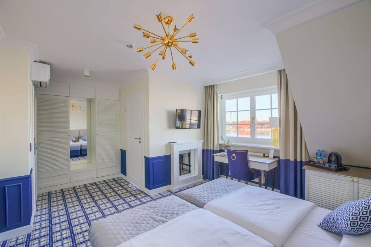 A hotel room with two beds, a desk, a chair, a TV, and a window with curtains.