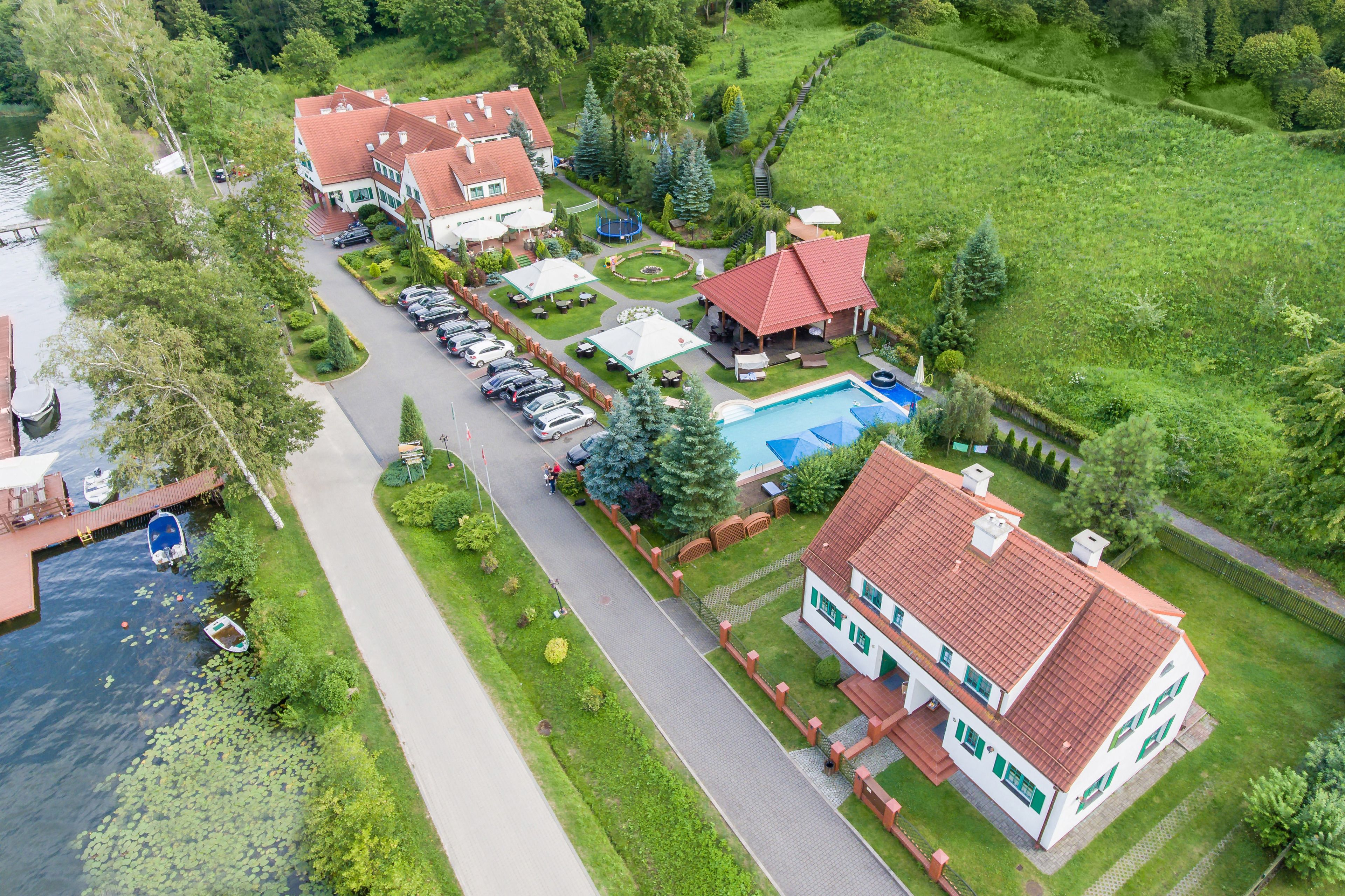 A residential property with a swimming pool, multiple houses, and a dock by the water.