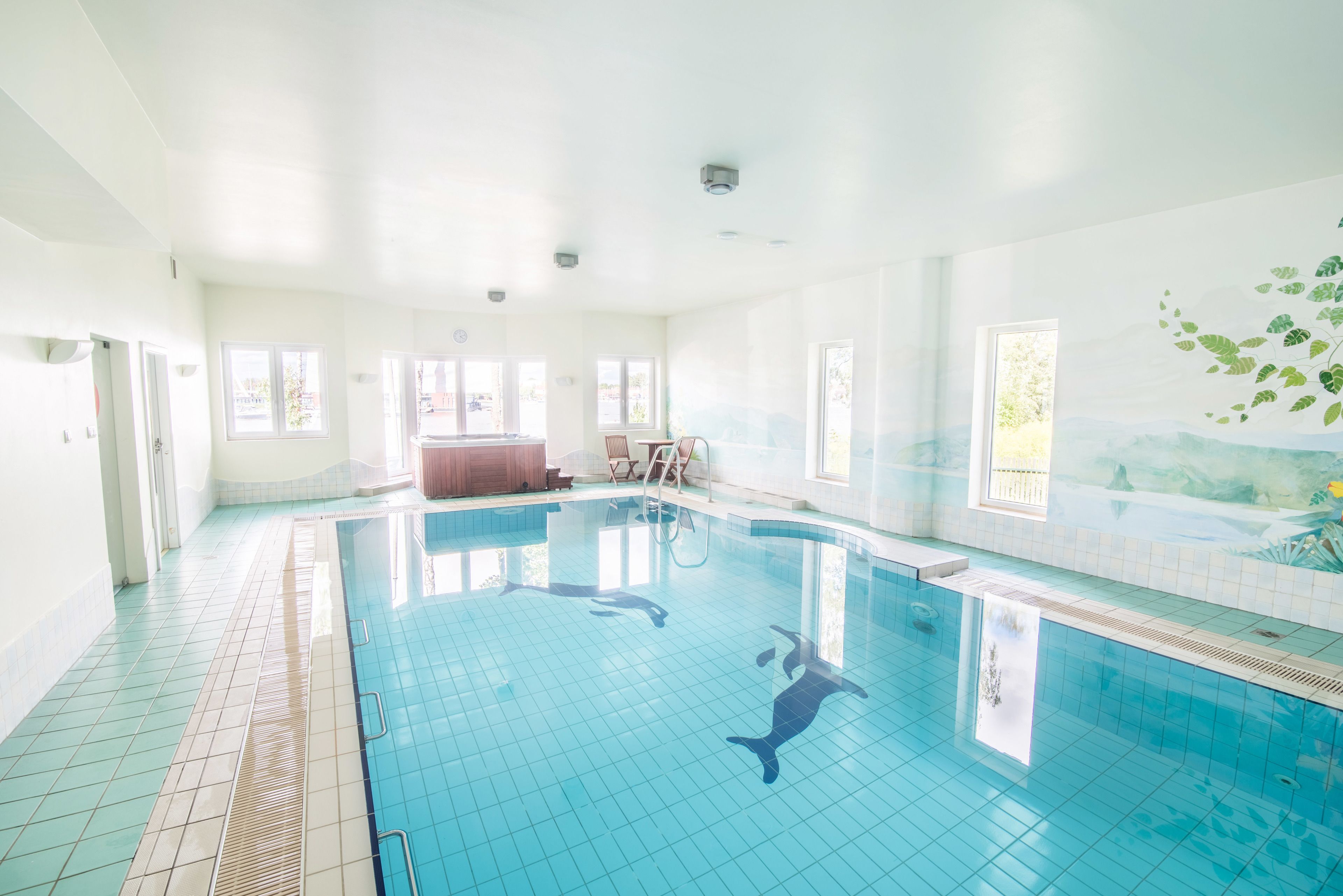 A large indoor swimming pool with clear blue tiles, a hot tub, and a mural of a forest on the wall.