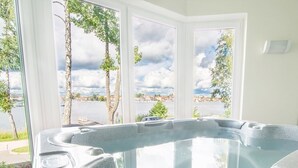 A hot tub with a view of a body of water and trees through large windows. - Hotel Amax (Mikolajki)