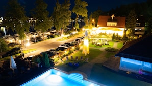 A nighttime view of a resort with a swimming pool, lounge chairs, and a parking area. - Hotel Amax (Mikolajki)