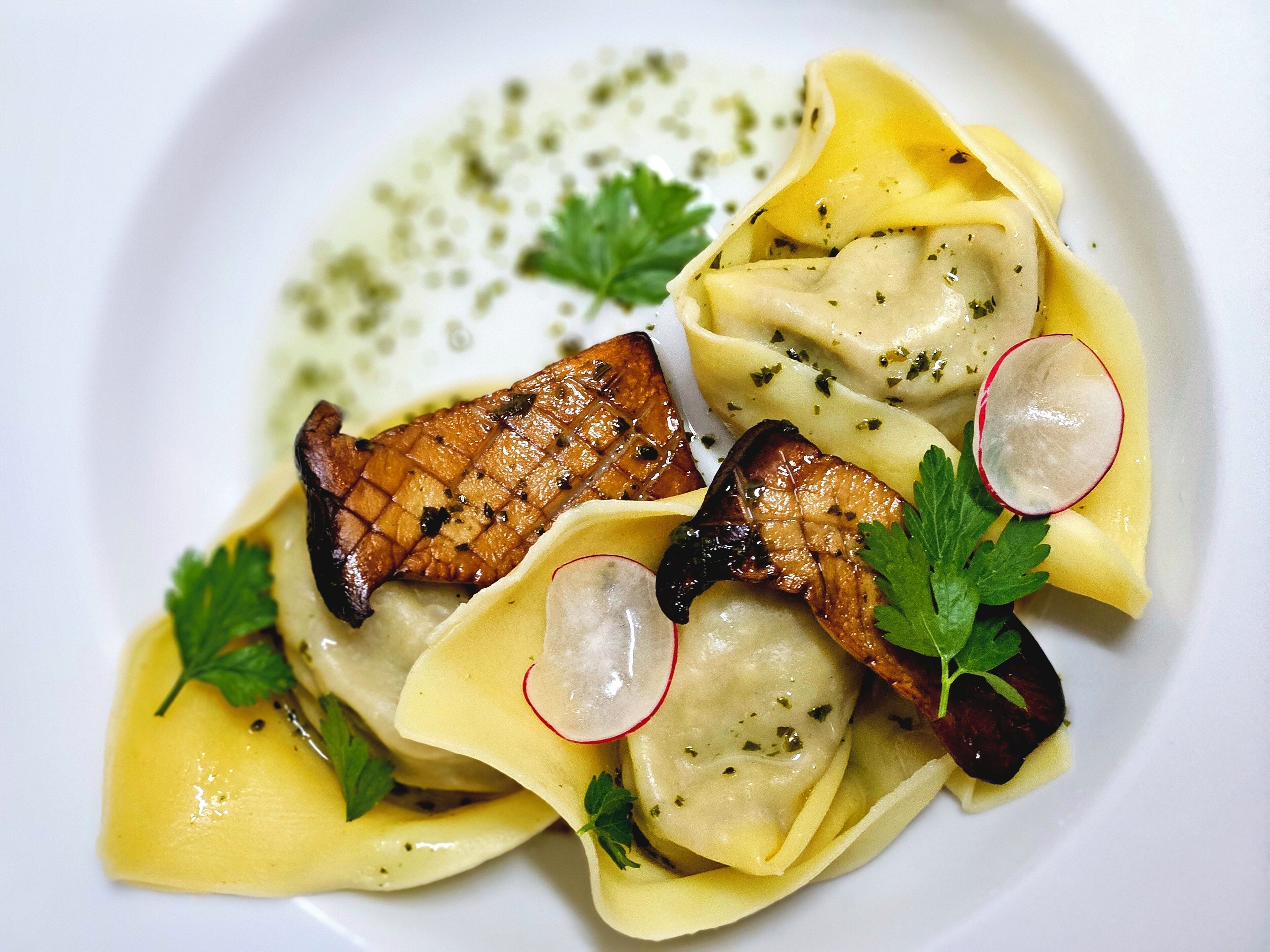 A plate of ravioli with a creamy sauce, garnished with radish slices and parsley.
