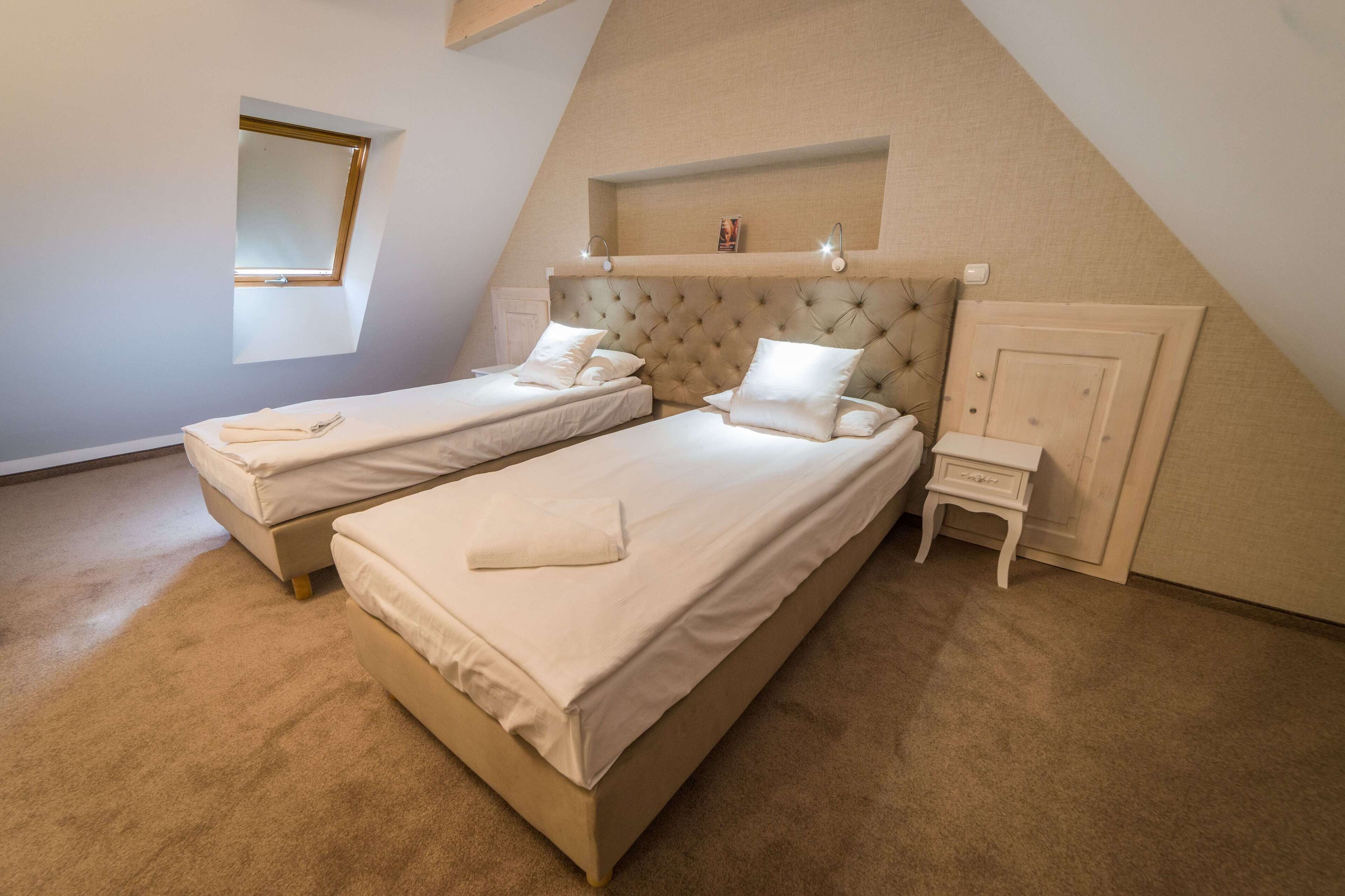 A bedroom with two beds, a small bedside table, a nightstand, a mirror, and a shelf above the beds.