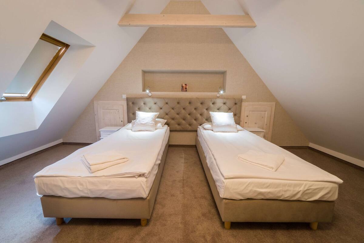 A bedroom with two single beds, a large window, and a sloped ceiling.
