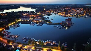 An aerial view of a lakeside town with a marina, residential buildings, and a bridge in the background. - Hotel Amax (Mikolajki)