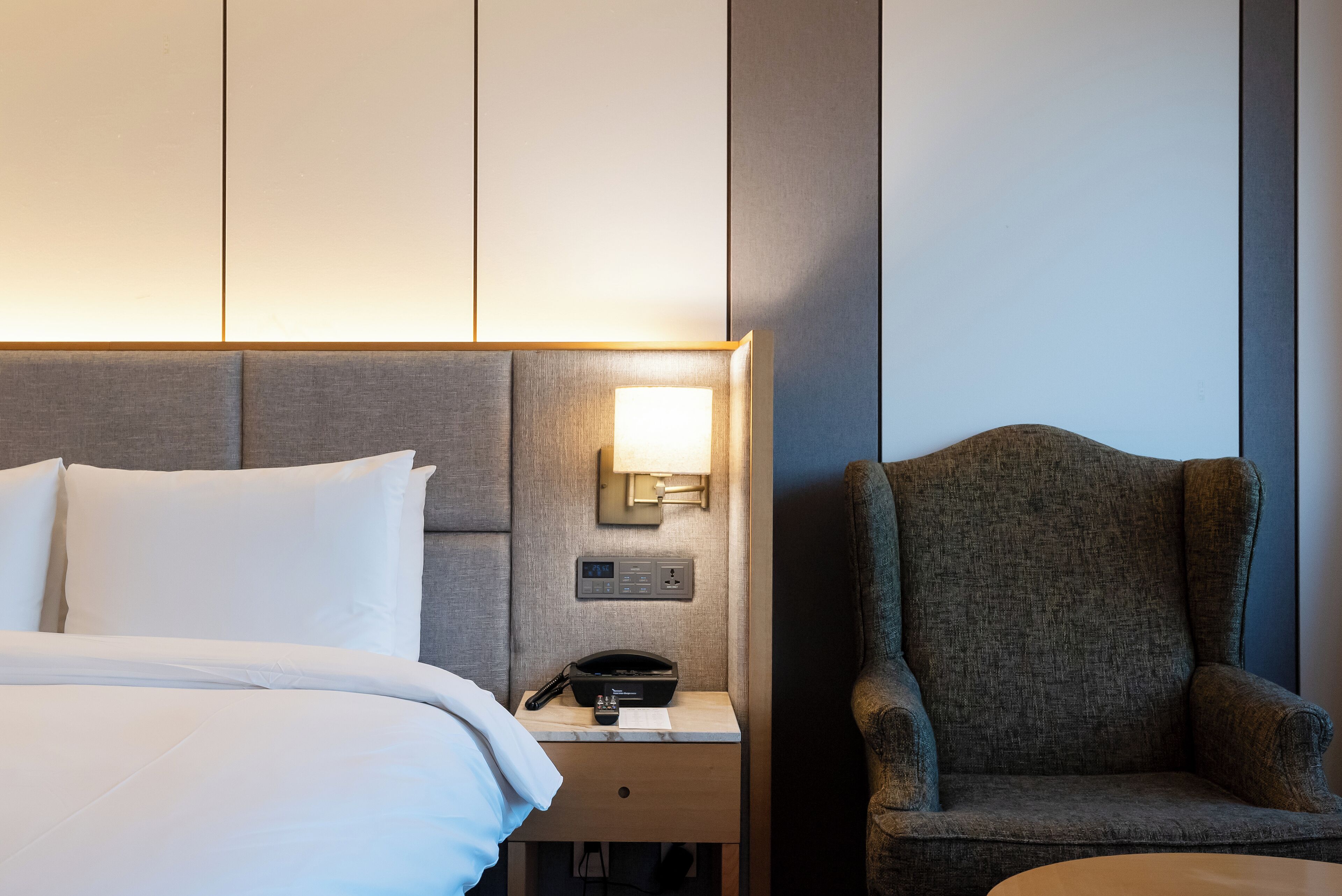 A hotel room with a bed, bedside table with a lamp, a phone, and a chair.