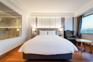 Una habitación de hotel moderna con una cama grande, mesitas de noche, una silla y vistas a la ciudad.