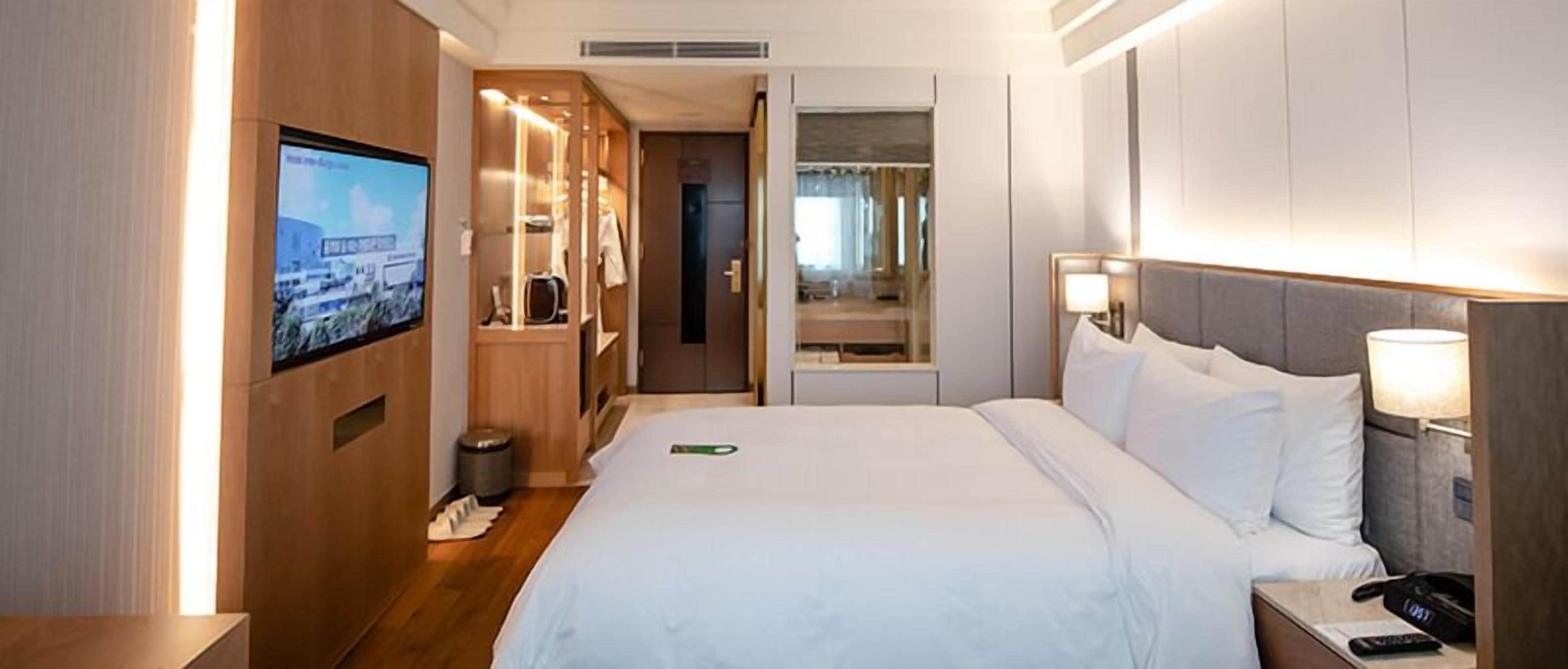 A hotel room with a bed, a TV, a mirror, and a bedside table.