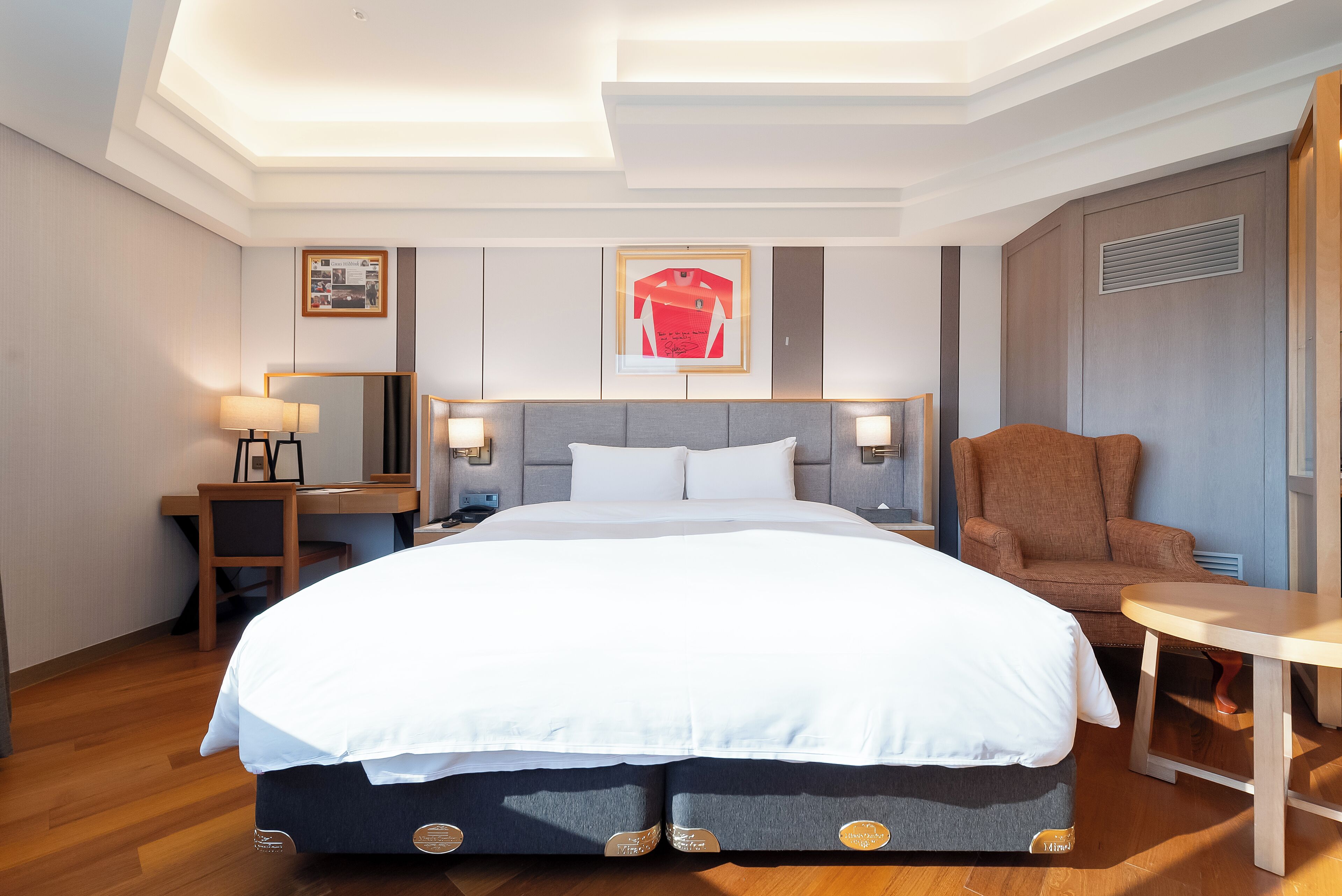 Una habitación de hotel con una cama grande, un escritorio con una silla, una mesita pequeña y un sillón marrón.
