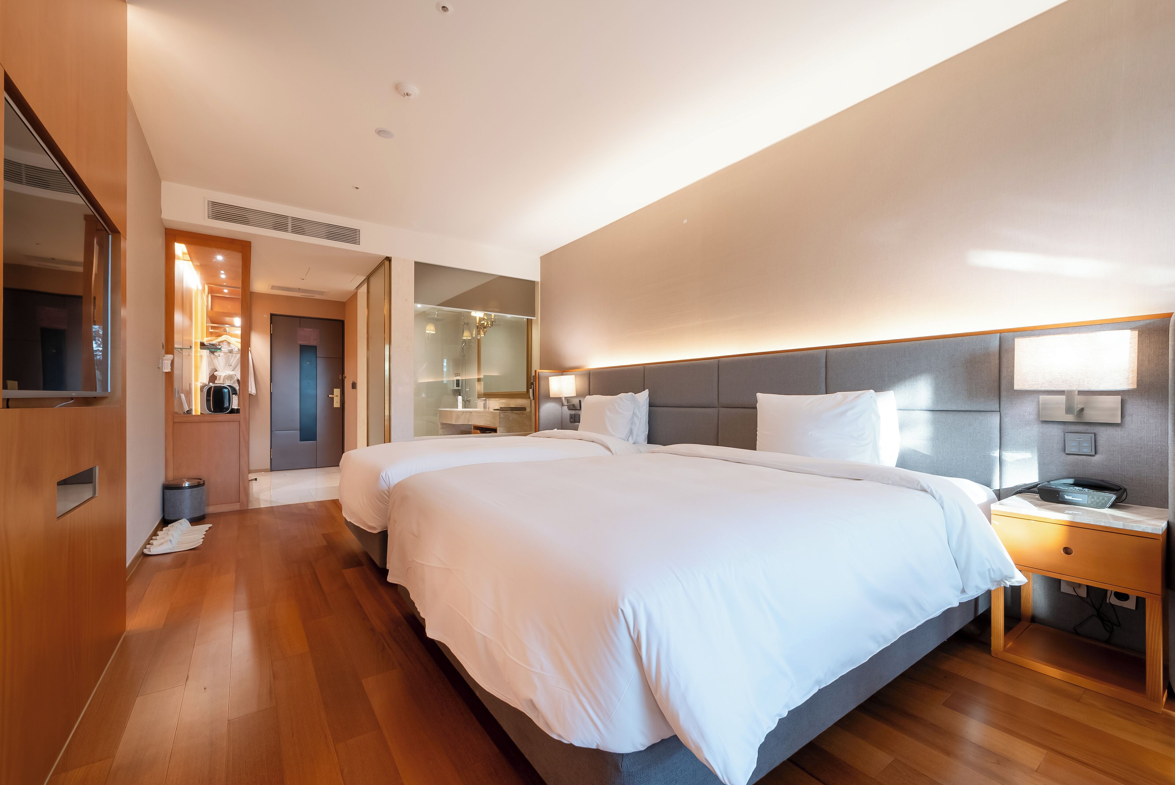 A modern hotel room with a large bed, bedside tables, a mirror, and a wardrobe.