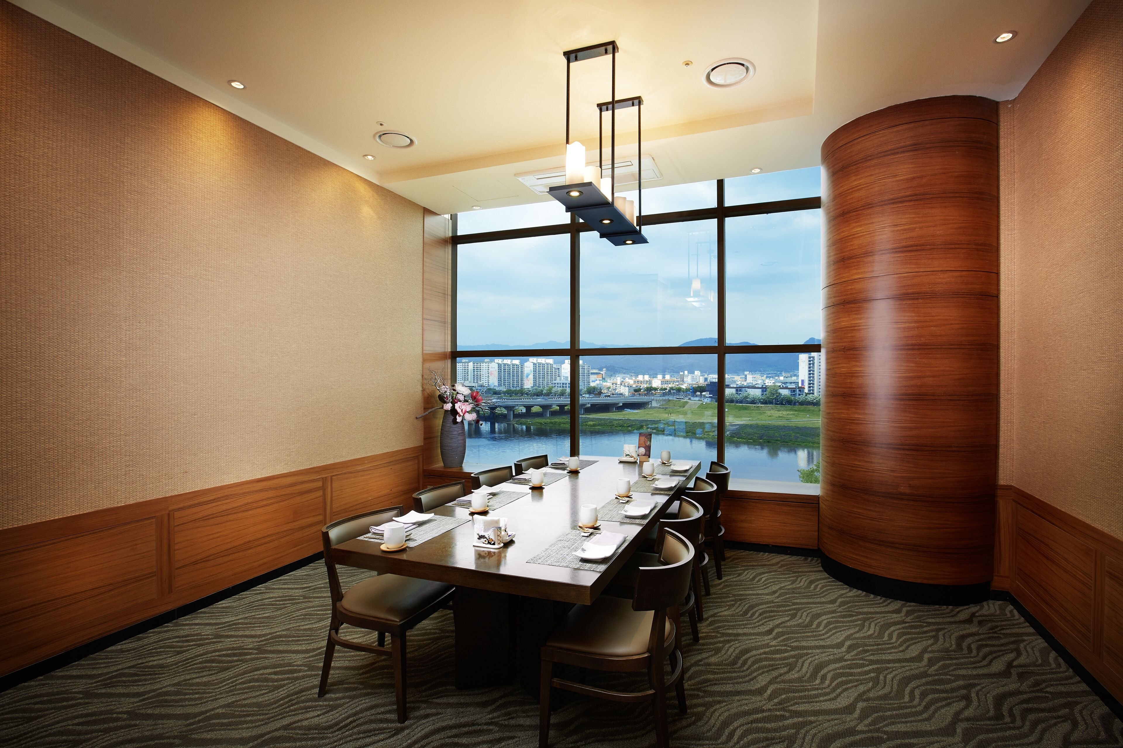 A conference room with a large table set for a meeting, large windows with a city view, and a modern ceiling design.