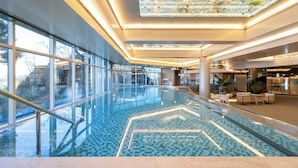 Una piscina interior moderna con barandillas de vidrio, un diseño geométrico de azulejos y un techo con tragaluces.