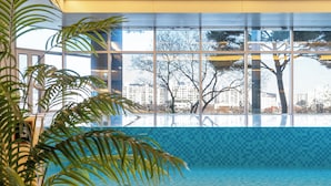 An indoor swimming pool with a tiled floor, large windows, and indoor plants.