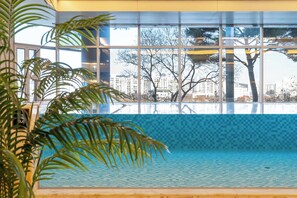 An indoor swimming pool with a tiled floor, large windows, and indoor plants.