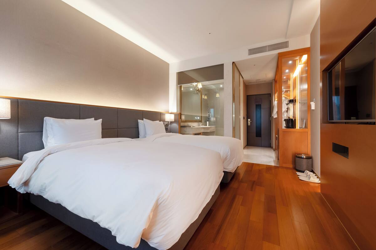 A modern hotel room with two beds, a large mirror, and a wooden floor.