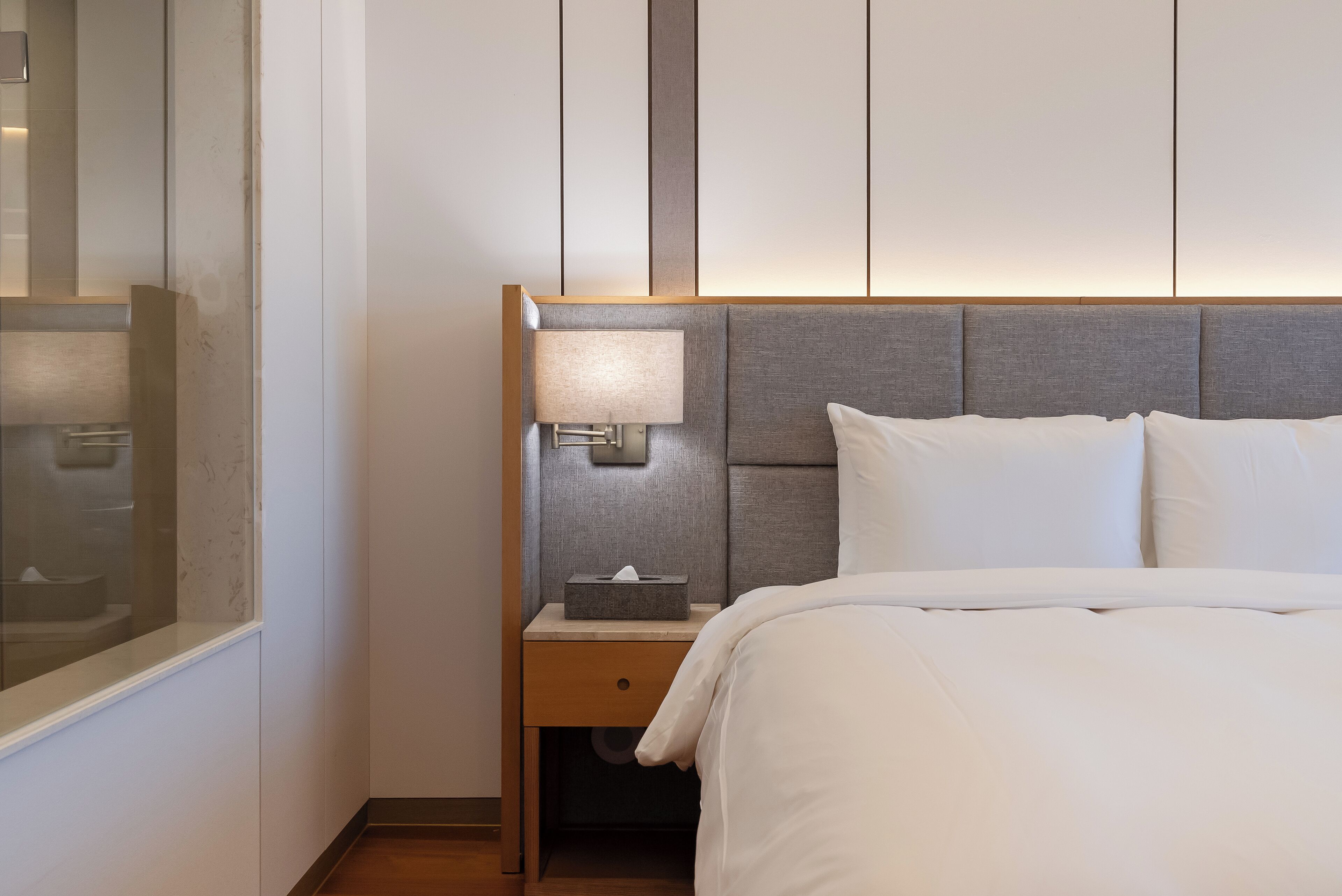 A hotel room with a large bed, a nightstand with a lamp, and a mirror on the wall.