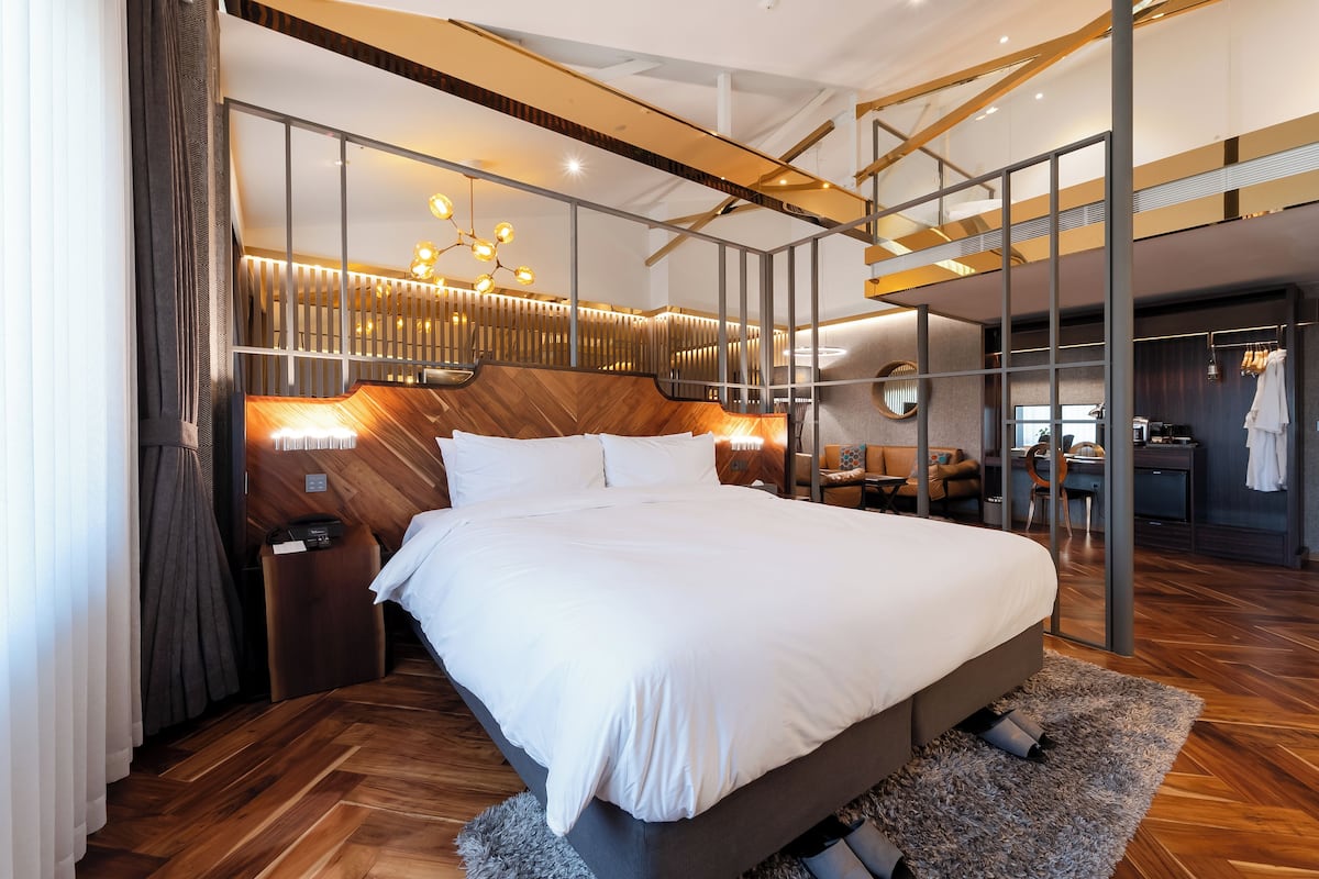 A modern hotel room with a large bed, a wooden headboard, a desk, and a wardrobe.